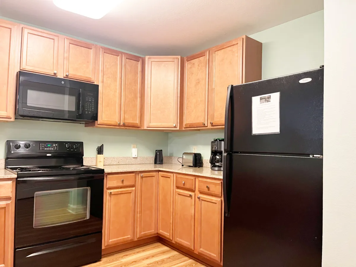 The image showcases a warm, inviting kitchen with sleek black appliances, rich wooden cabinets, and a stunning granite countertop—perfect for gathering, cooking, and creating memories. The space promises home-cooked meals and cozy moments, evoking comfort and togetherness.