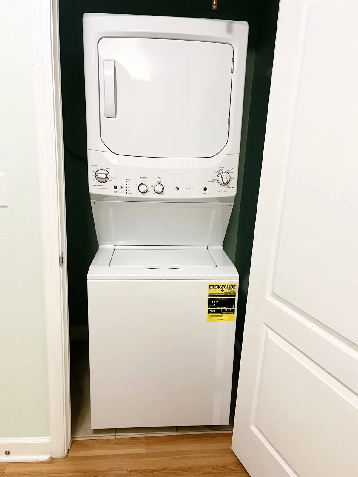 This practical and tidy interior image highlights a stacked washer and dryer with an energy guide label, surrounded by white cabinetry and organized flooring. The scene conveys the convenience and efficiency of having in-unit laundry appliances available in the home.